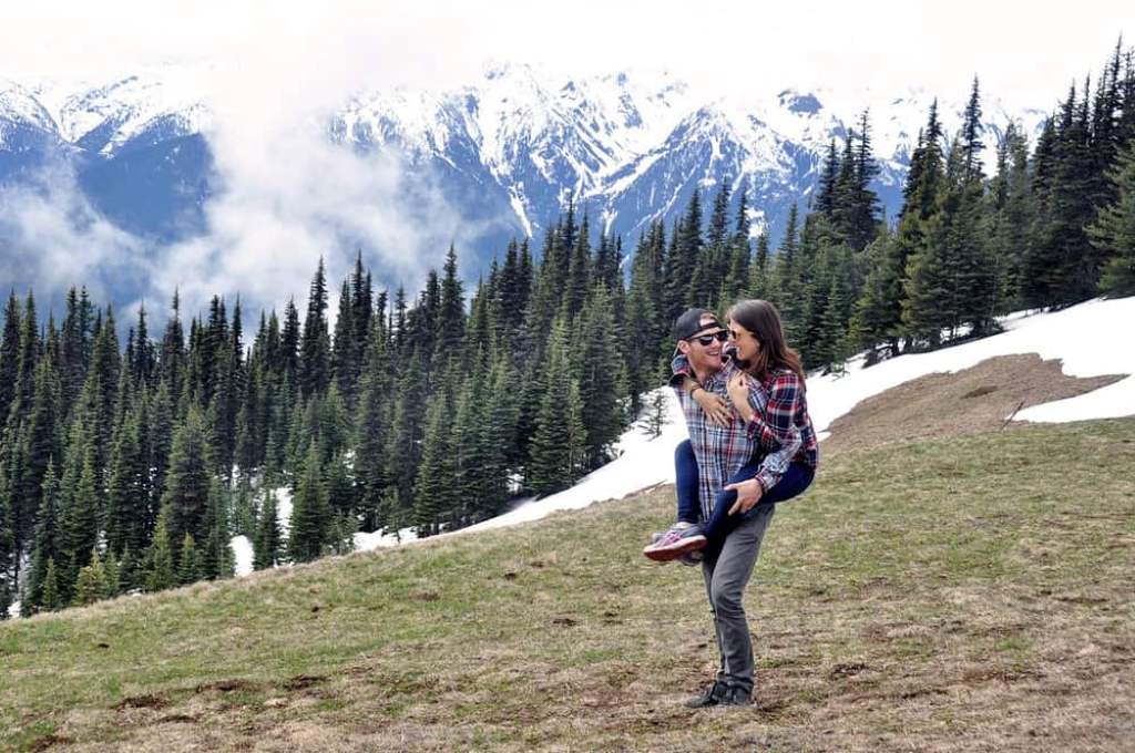 Hiker stands atop Hurricane Ridge in Olympic National Park, gazing at snow-capped peaks under a clear blue sky.